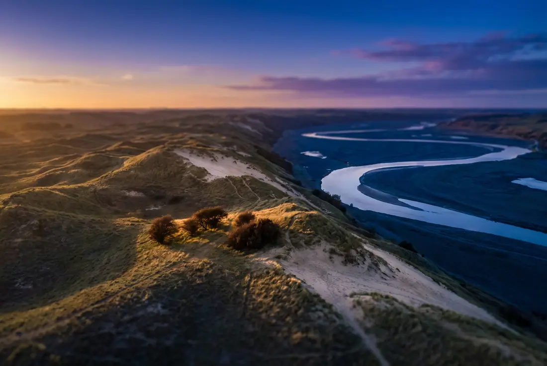 Grass-covered sand hills above a winding river valley in the last light of the day