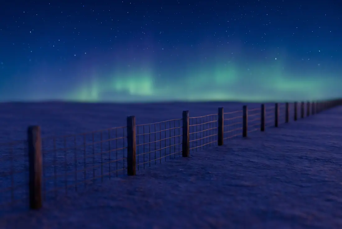 Ciel de nuit étoilé avec une faible aurore verte au-dessus de la prairie plate et d'une clôture