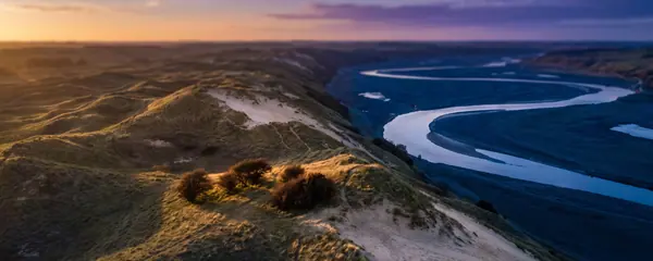 Collines de sable couvertes d'herbe au-dessus d'une vallée de rivière sinueuse, dans la dernière lumière du jour